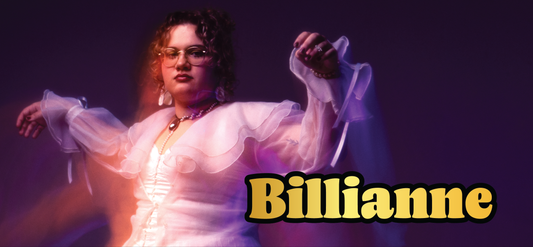 A woman with curly hair, glasses, and ruffled sheer sleeves poses confidently against a purple background. The bold yellow text Billianne is displayed in the lower right corner.