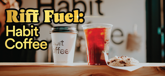 Two coffee drinks, one hot in a to-go cup and one iced in a plastic cup, sit on a wooden counter next to a cookie. Bold yellow text reads, Riff Fuel: Habit Coffee. The background is softly blurred.