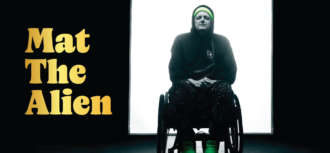 A person in a wheelchair, wearing a hoodie and neon green hat and shoes, sits in front of a bright white background. Large yellow text on the left reads, Mat The Alien.